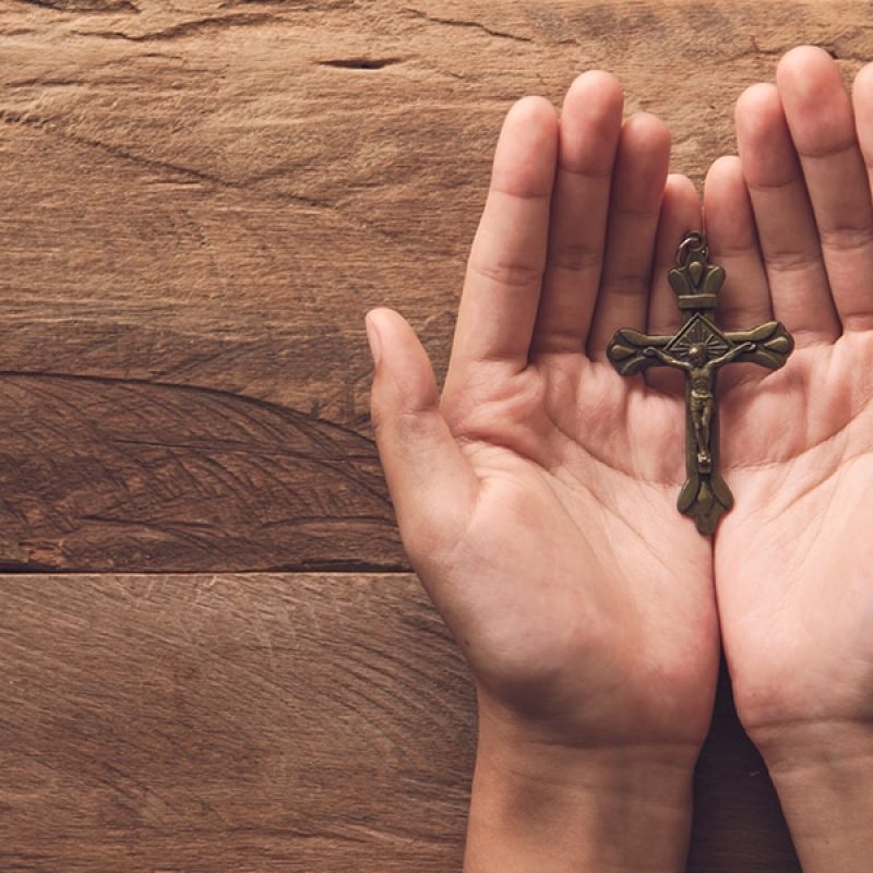 Open hands holding a metal cross
