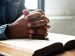Folded hands in prayer over a open Bible