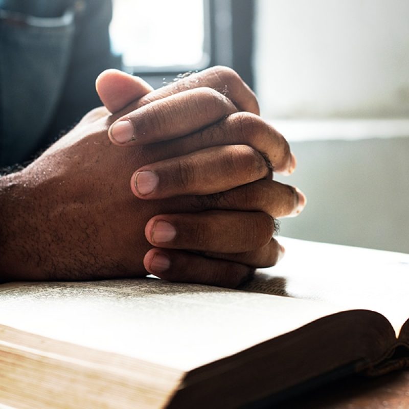 Folded hands in prayer over a open Bible