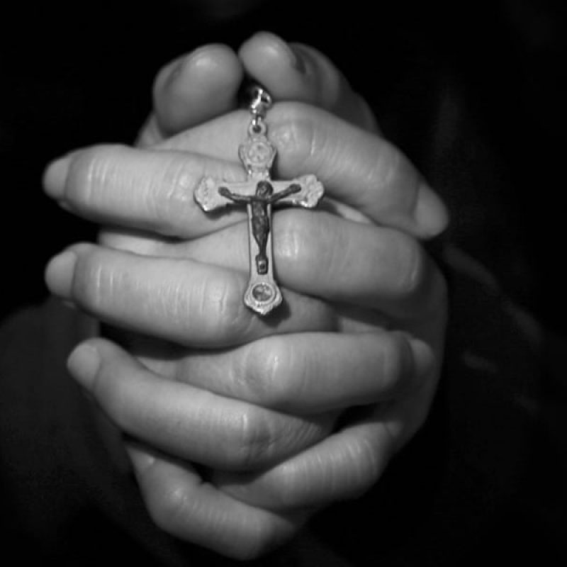 hands folded in prayer while holding a rosary