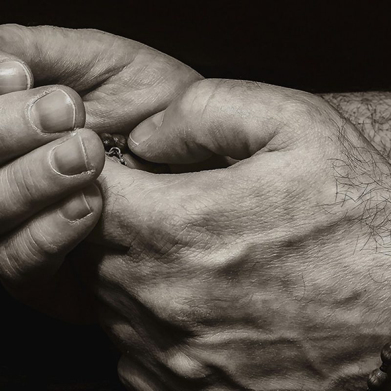 hands folded in prayer while holding a rosary