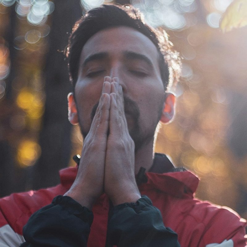 man reflecting with, taking a deep breath with hands folded.