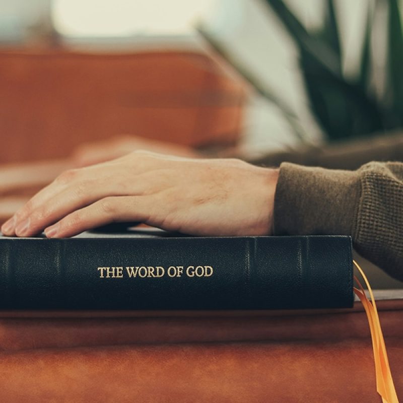 man resting hand on Bible while sitting in a chair