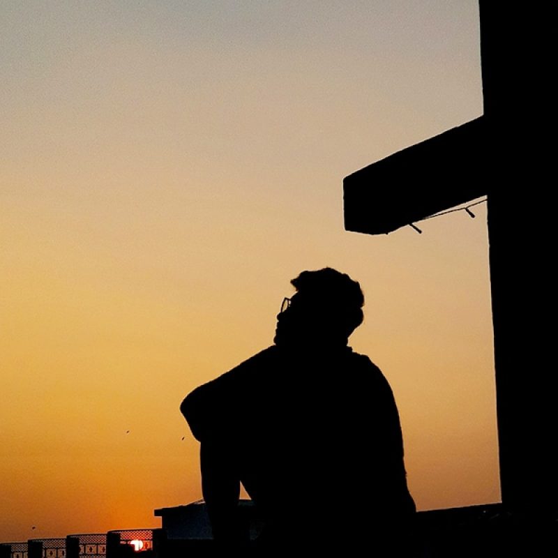 a man sitting in front of a cross with a sunset in the background