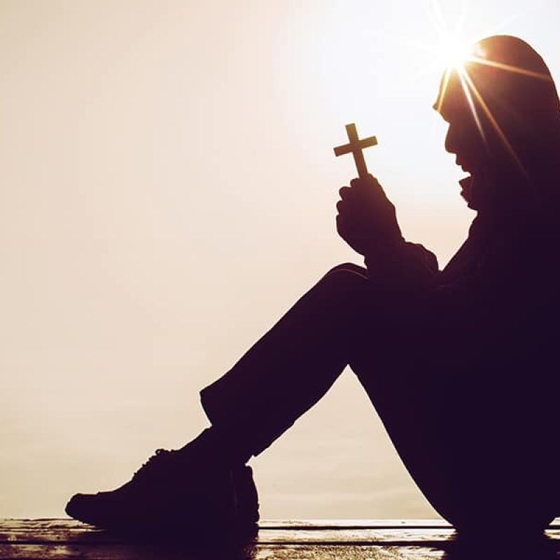 man sitting in meditation while holding a cross with both hands.
