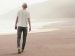 man walking along beach on the ocean with cliffs in the background.
