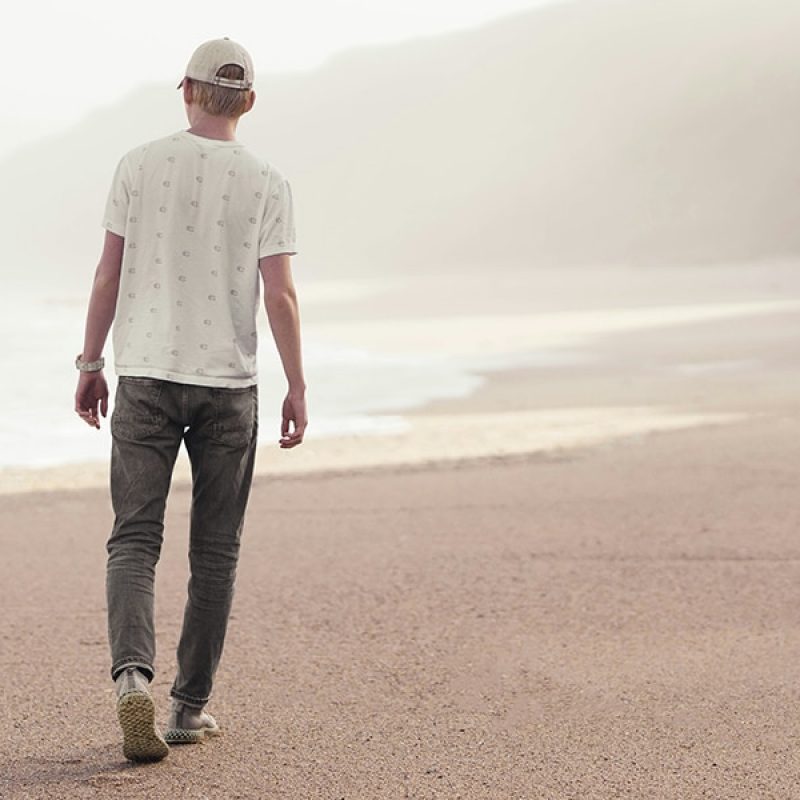 man walking along beach on the ocean with cliffs in the background.