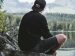 man sitting quietly on a rock by a lake.
