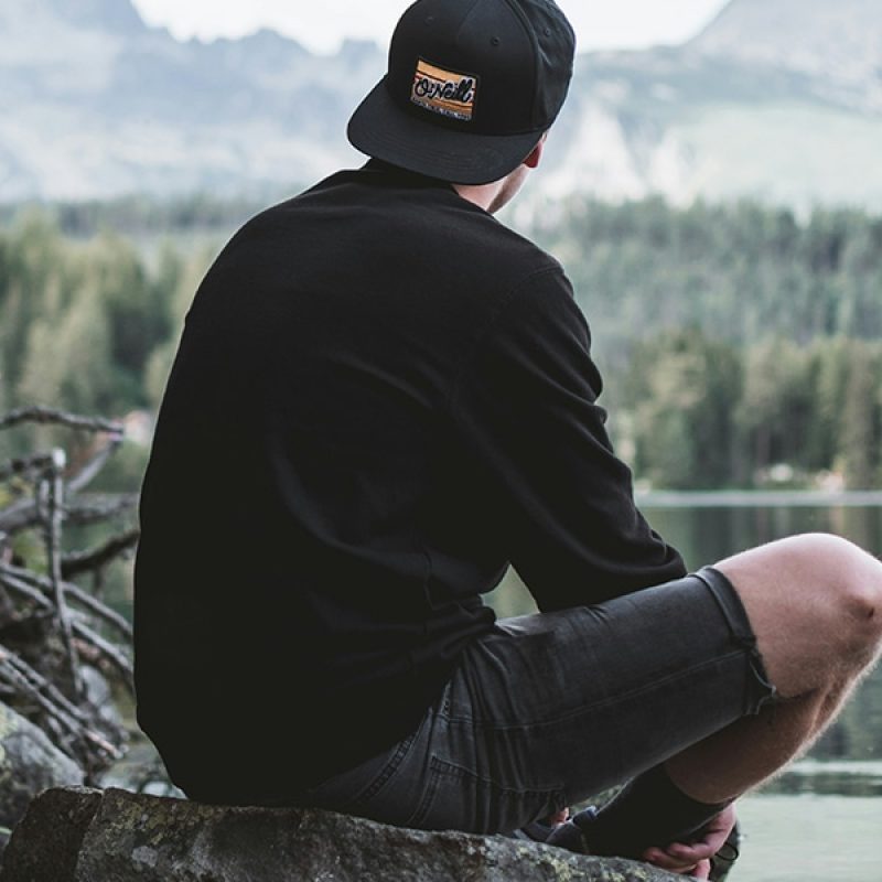 man sitting quietly on a rock by a lake.