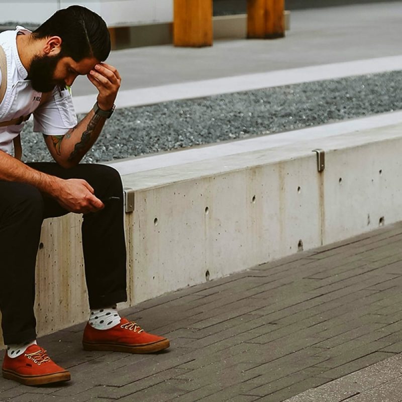 man being sad, resting his head in his hand, sitting outside