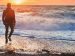 man walking on beach while waves crashing