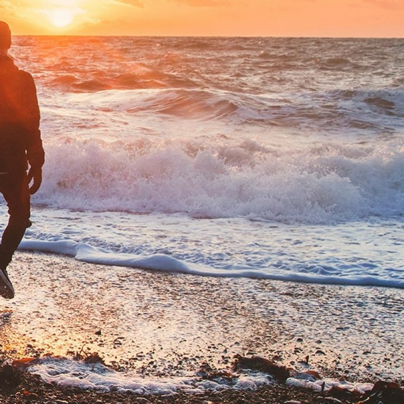 man walking on beach while waves crashing