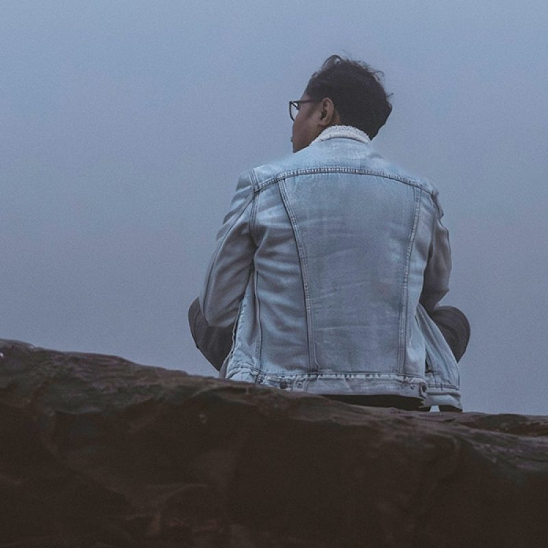 man sitting quiet on a rock in fog