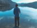 man standing by a lake and enjoying the view of the mountains.
