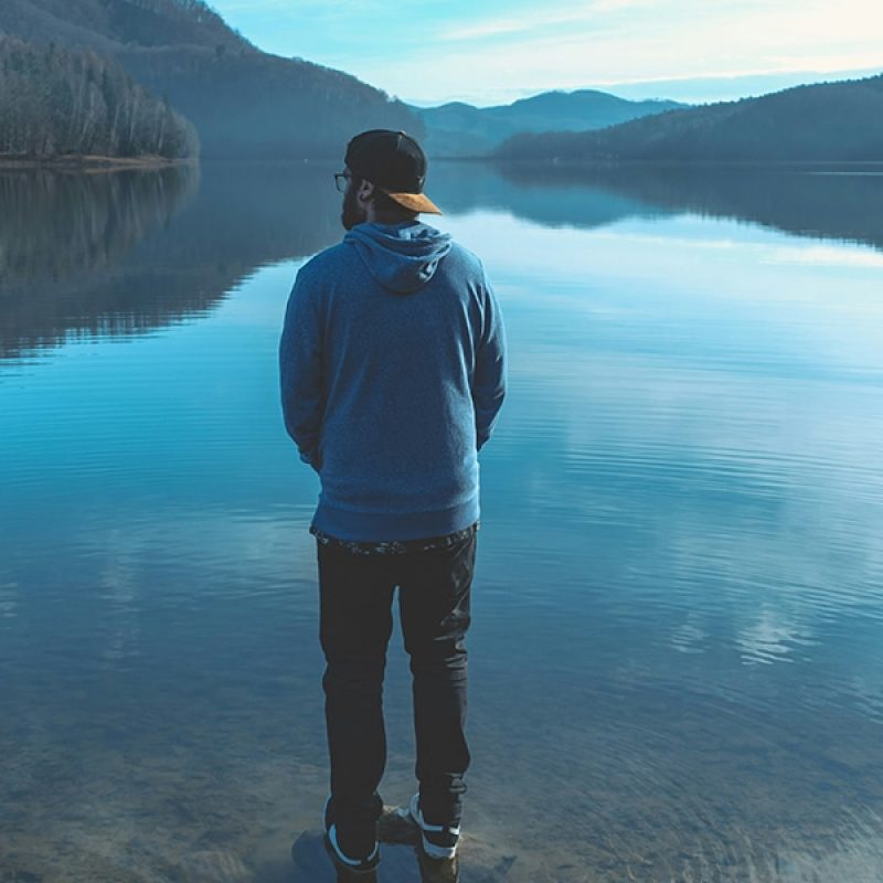 man standing by a lake and enjoying the view of the mountains.