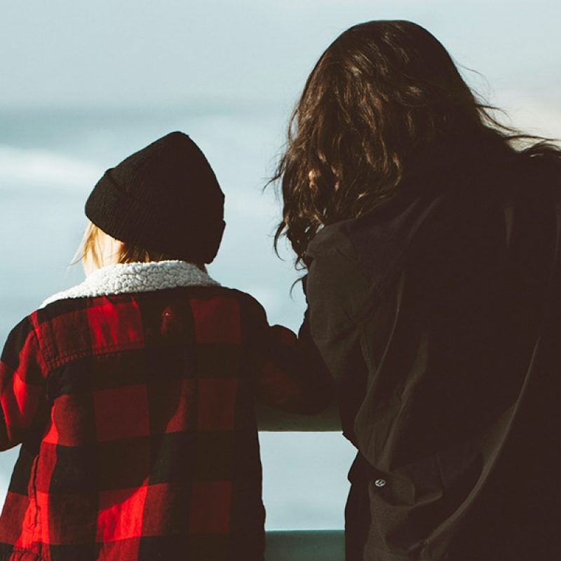 mother watching over her child while standing at a peer at the ocean.