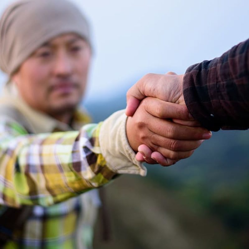 person reaching out a hand to help pull a man up.