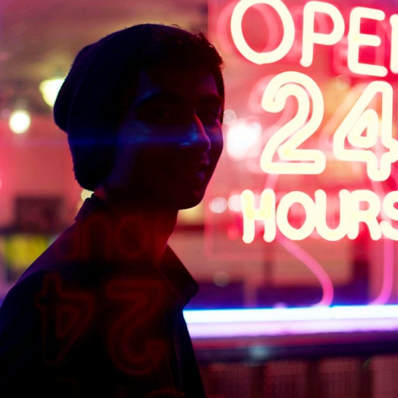 person in front of a open twenty four hours neon sign.