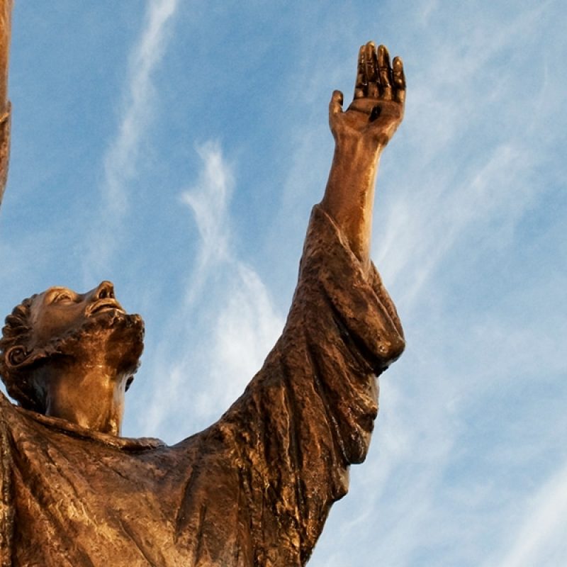 A statue of St. Francis with raised hands and looking into the sky