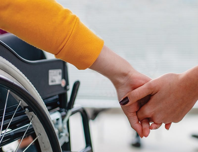 Person in chair and person in wheelchair holding hands