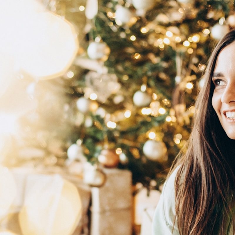 the celebration of christmas; woman on her cellphone in front of a Christmas tree.