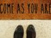 shoes in front of a welcome rug with the words "Come as you are" printed on it.