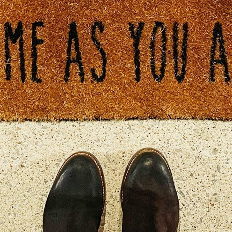 shoes in front of a welcome rug with the words "Come as you are" printed on it.