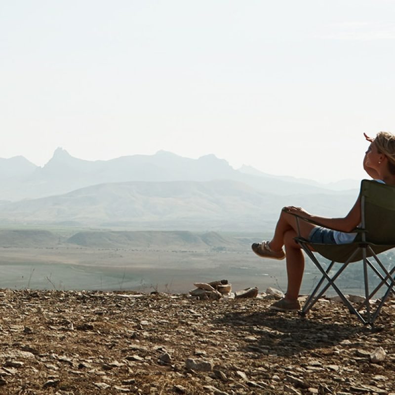 woman sitting in a chair outside with mountains in the background.