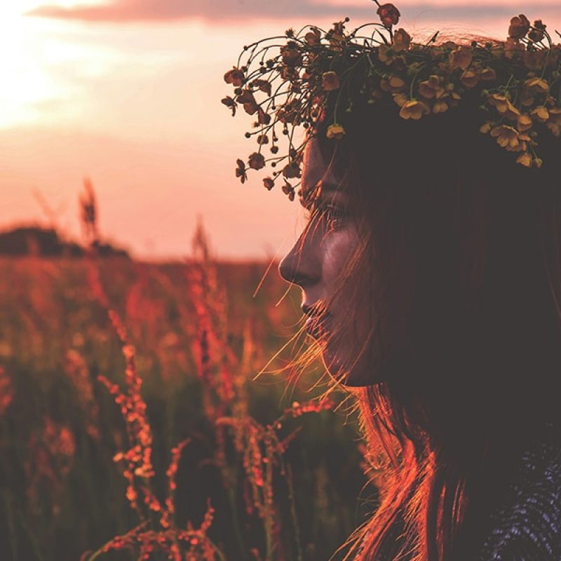 woman wearing a flower crown standing in a field during sunset.