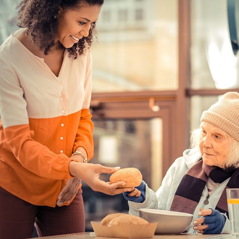 woman helping homeless woman with food,