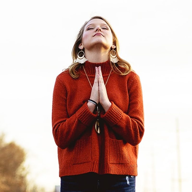 woman hands folded and eyes closed in prayer with a hopeful expression on her face.