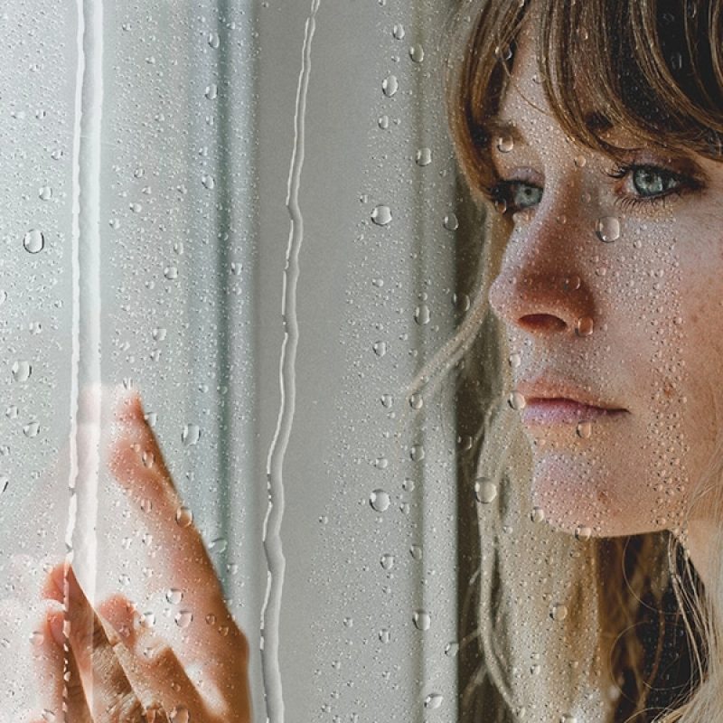 sad woman behind a window with water drops.